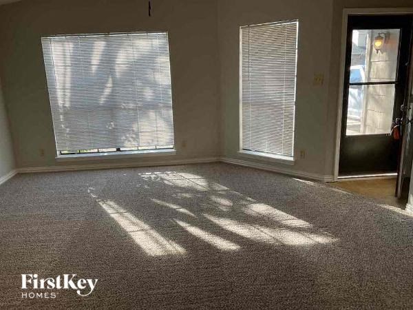A room with a carpeted floor, two windows with blinds, and a door.