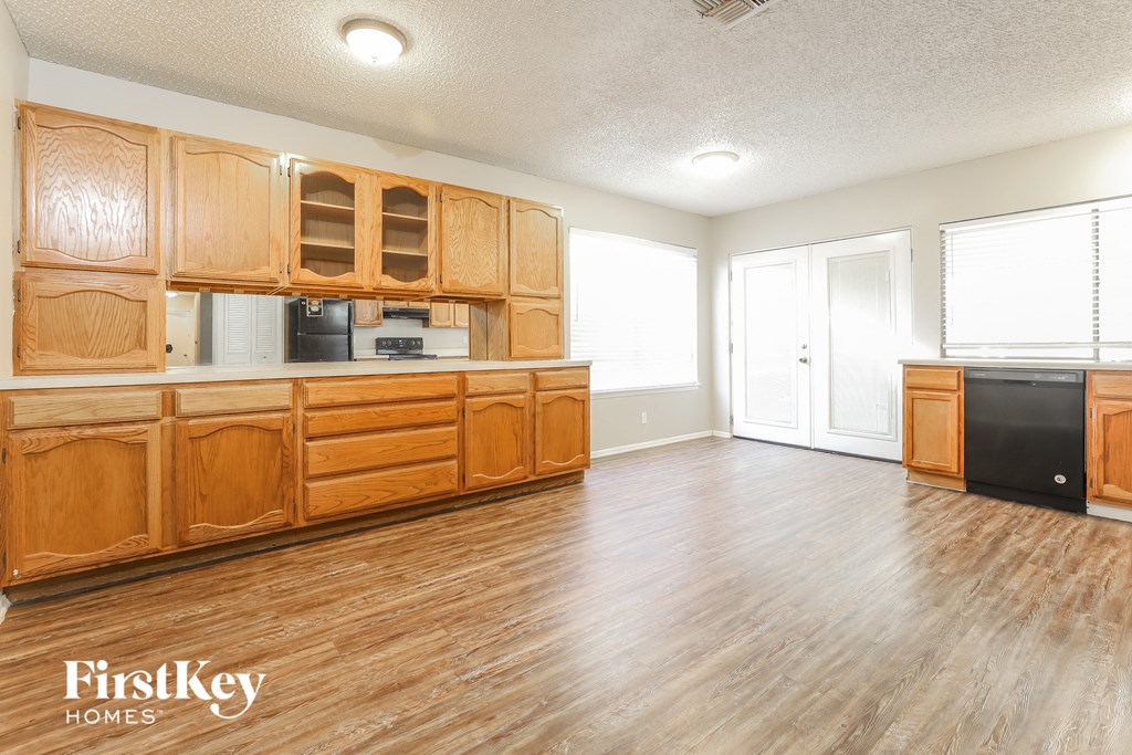 the kitchen and living room of a house with wood floors and wooden cabinets
