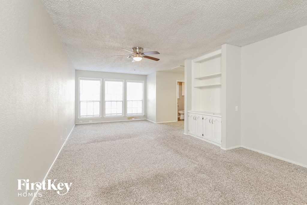 a spacious living room with carpet and a ceiling fan