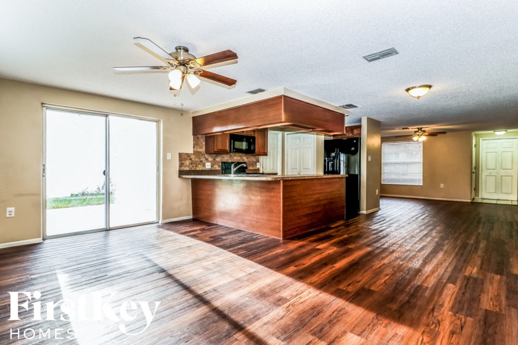 an empty living room with a kitchen and a ceiling fan