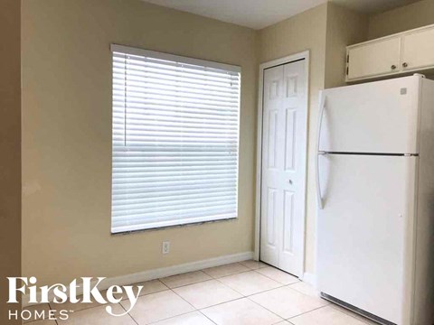 A white refrigerator is in a kitchen with a white door and a window with blinds.