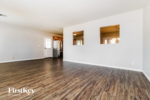 A spacious room with wooden flooring and white walls, with a refrigerator and a chandelier visible.