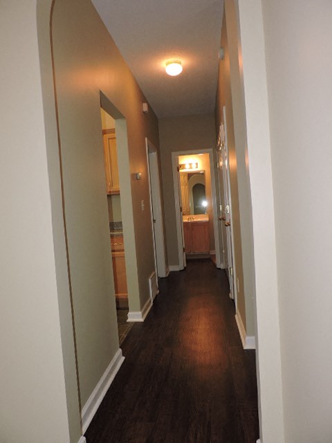 a hallway with a wood floor and white walls and a door way to a kitchen