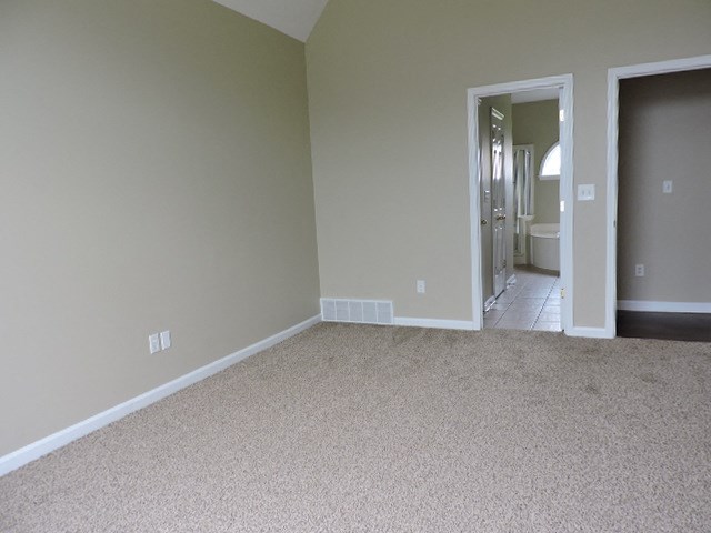 an empty living room with carpet and a door to a bathroom