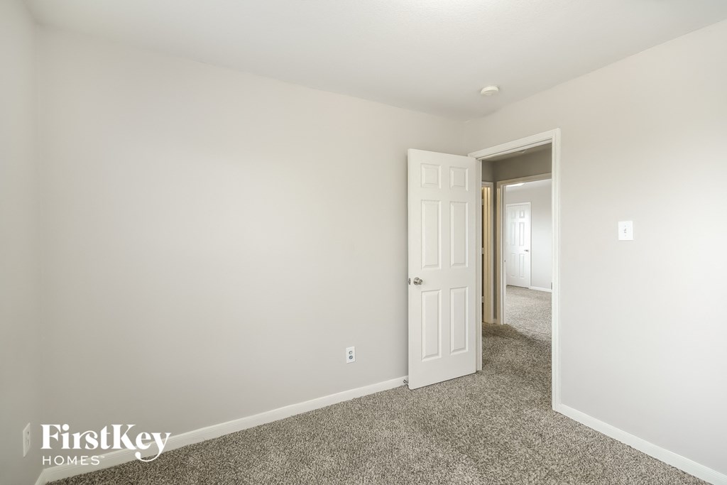 a bedroom with white walls and carpet and a door to a hallway