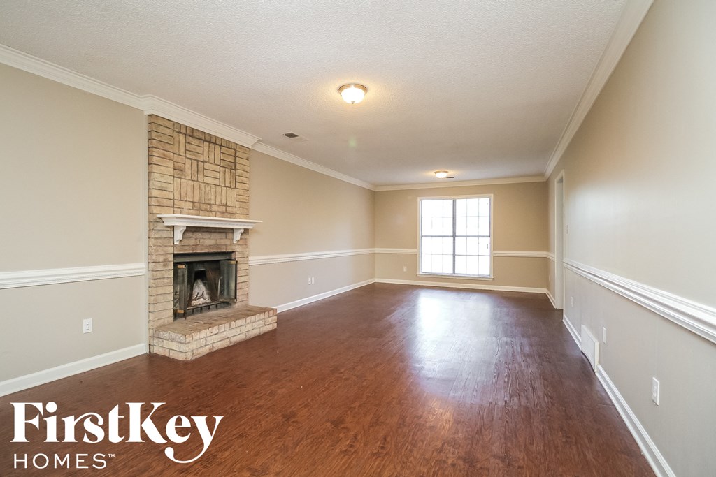 A large empty room with a fireplace and wood flooring.
