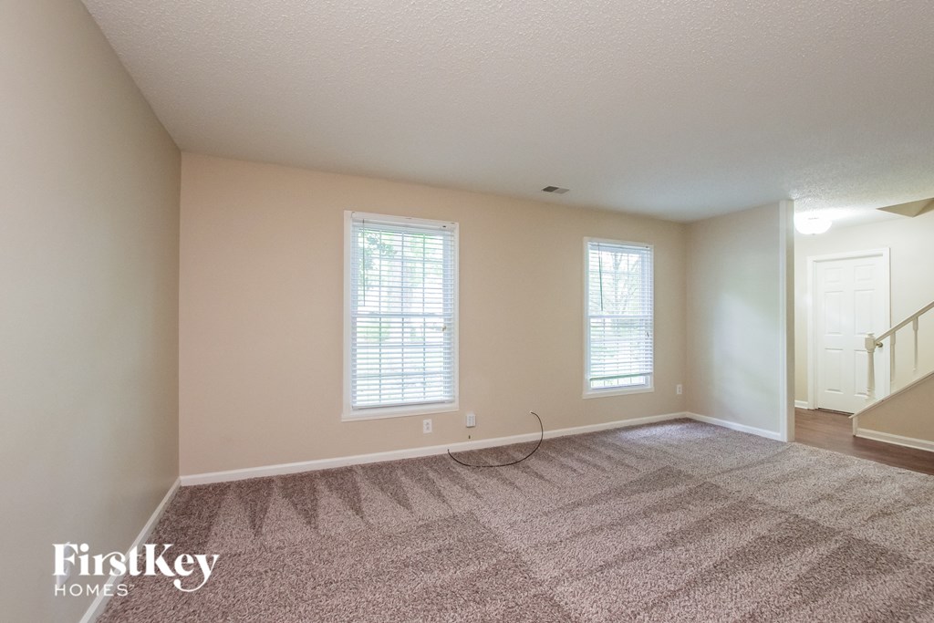 an empty living room with a carpeted floor and two windows