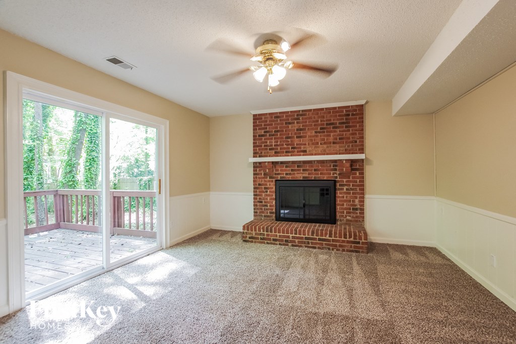 an empty living room with a brick fireplace and a ceiling fan