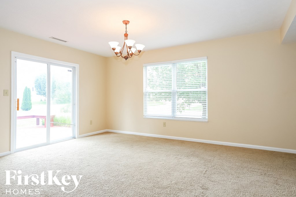 A room with a carpet floor, a chandelier, and a window with blinds.