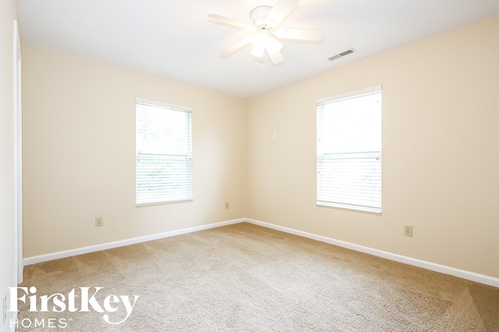 A room with a carpet floor, a ceiling fan, and two windows.