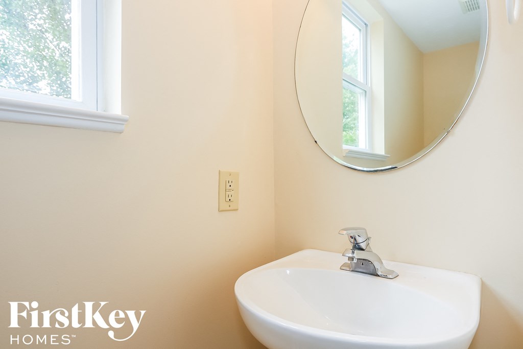 A white sink in a bathroom with a round mirror above it.