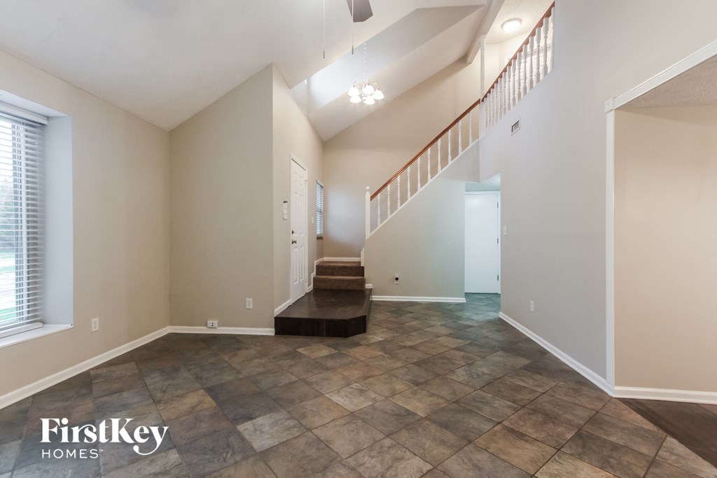 the living room and entryway of an empty home with tile floors and a staircase