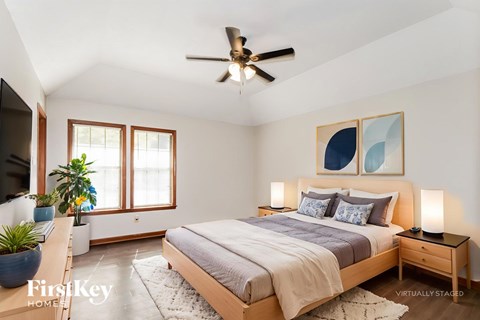 A bedroom with a bed, a ceiling fan, and a painting on the wall.