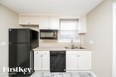 A black fridge and microwave in a kitchen with white cabinets.