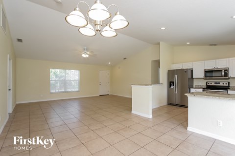 A spacious kitchen and living room with a white ceiling and tiled floor.