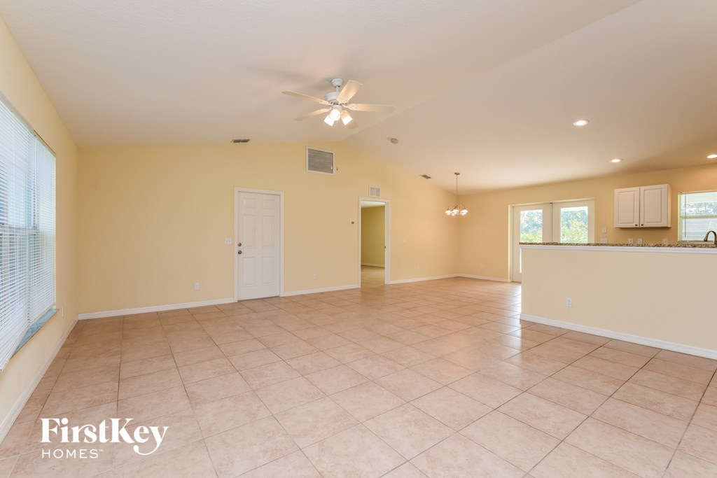an empty living room with a kitchen and a ceiling fan