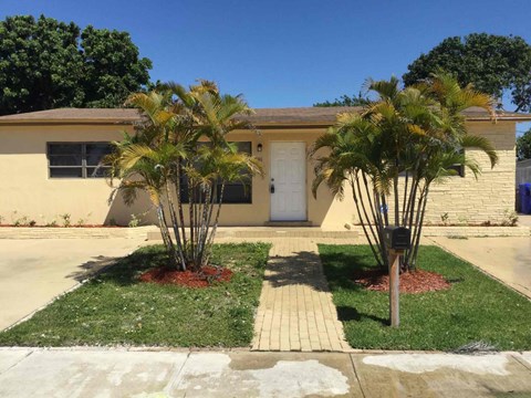 A house with a white door and two palm trees in front.