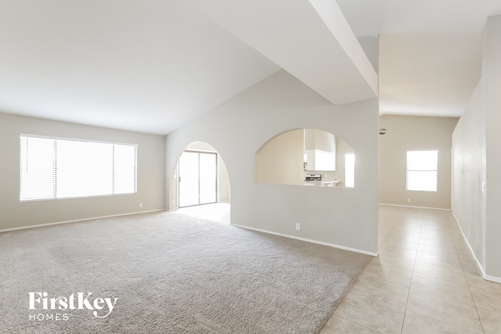 A spacious, empty room with a carpeted floor and large windows.