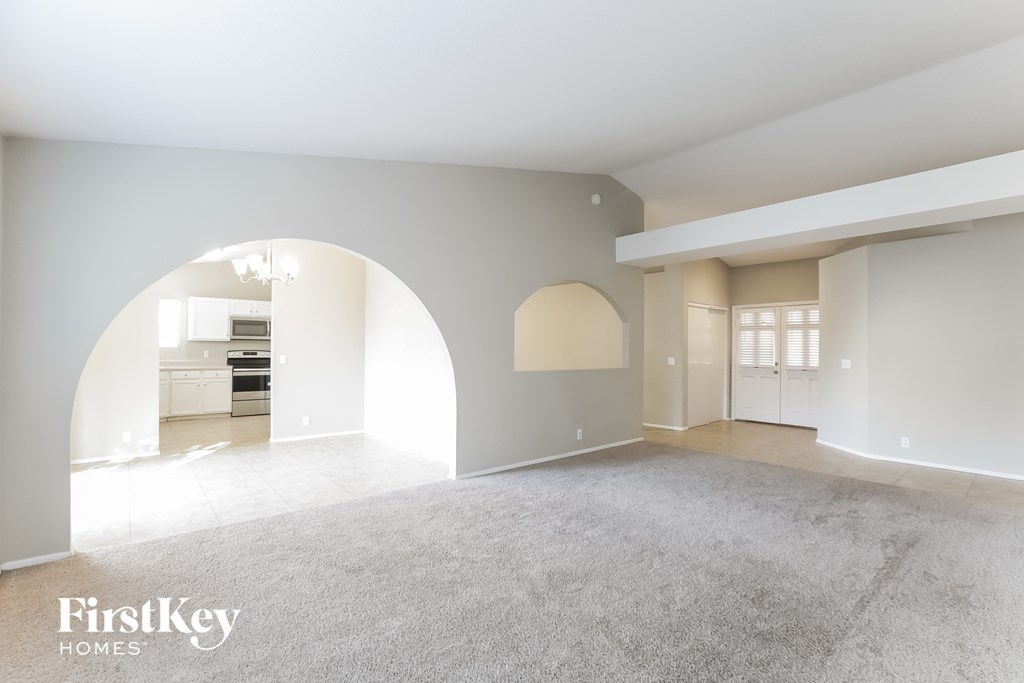 A spacious room with a carpeted floor and a large arched opening leading to another room.