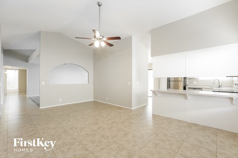 A spacious room with a fan and a kitchen area in the background.