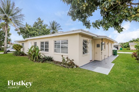 a small white house with a lawn and palm trees