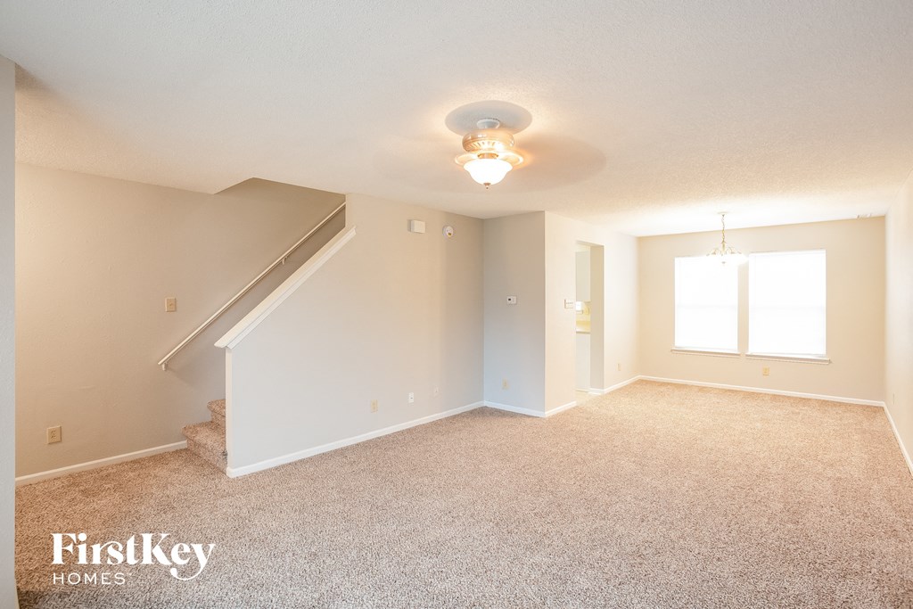 A carpeted room with a staircase and a window.