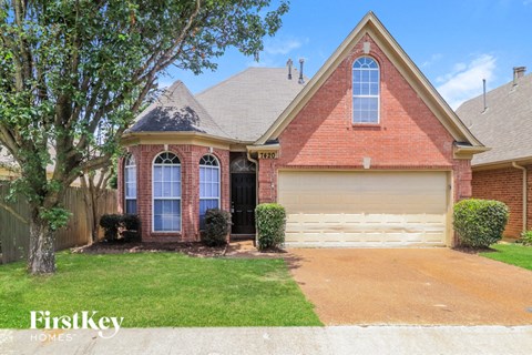 A brick house with a garage door and a tree in front.