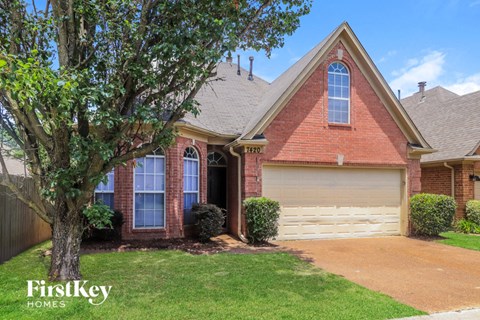 A red brick house with a white garage door and a tree in front.