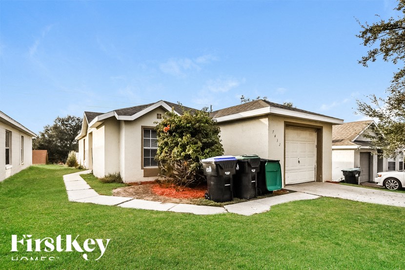 A white house with a green trash can in front of it.