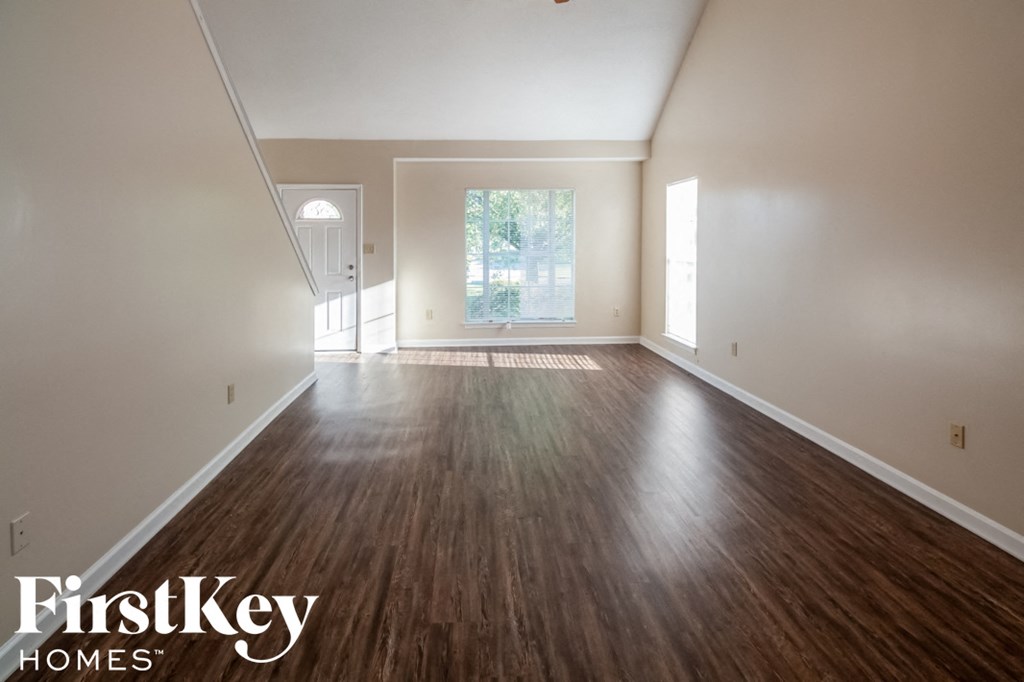 A room with wooden floors and white walls, with a window and a door visible.