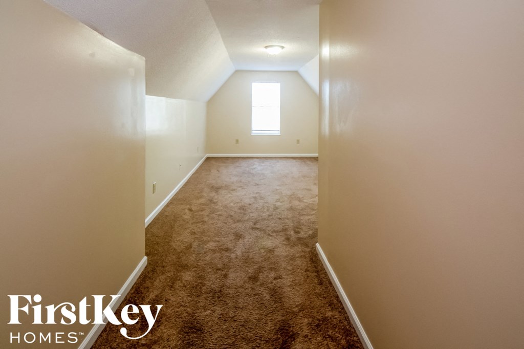 A long hallway with a carpeted floor and a window at the end.