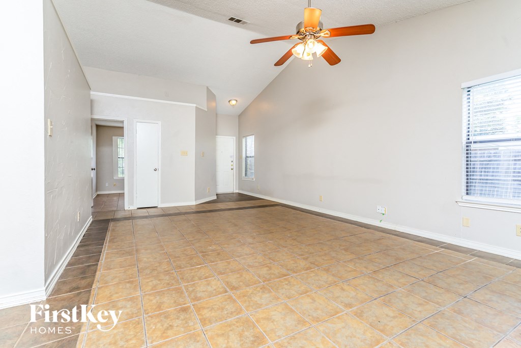 an empty living room with a ceiling fan and tile flooring