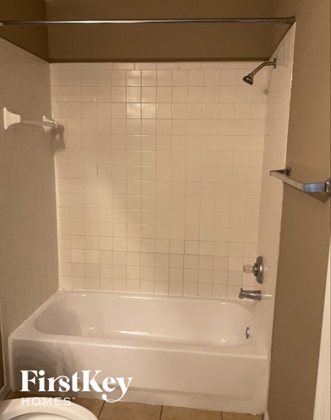 A white tiled bathroom with a bathtub and a shower head.
