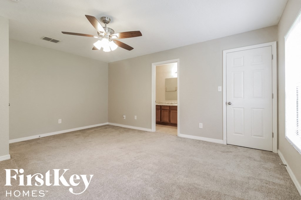 an empty living room with a ceiling fan and a door to a bathroom