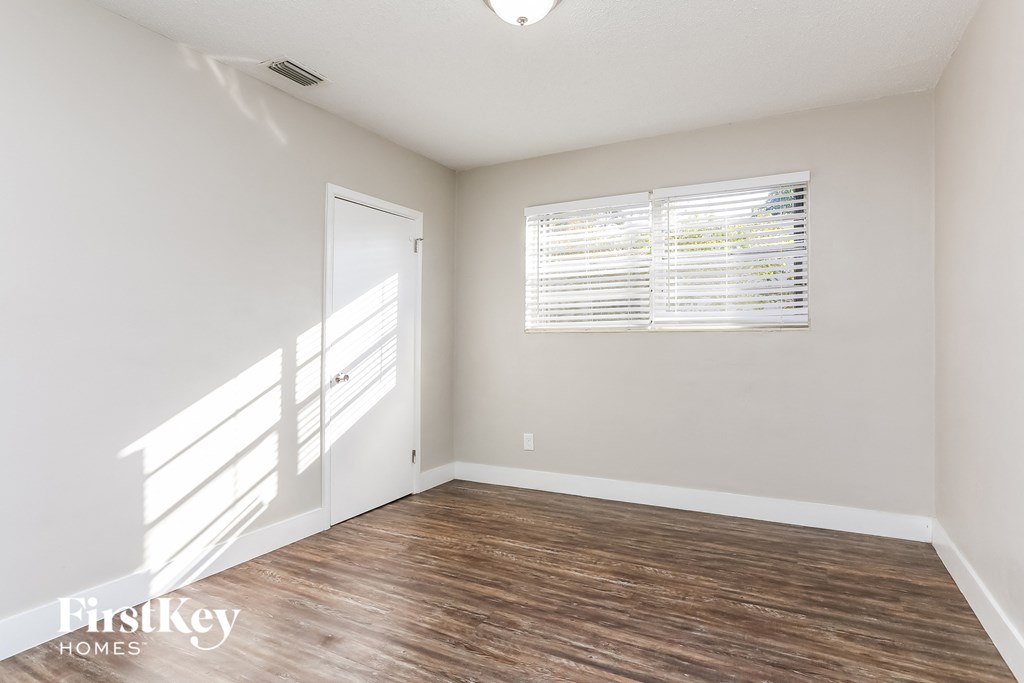 a bedroom with white walls and wood flooring and a window