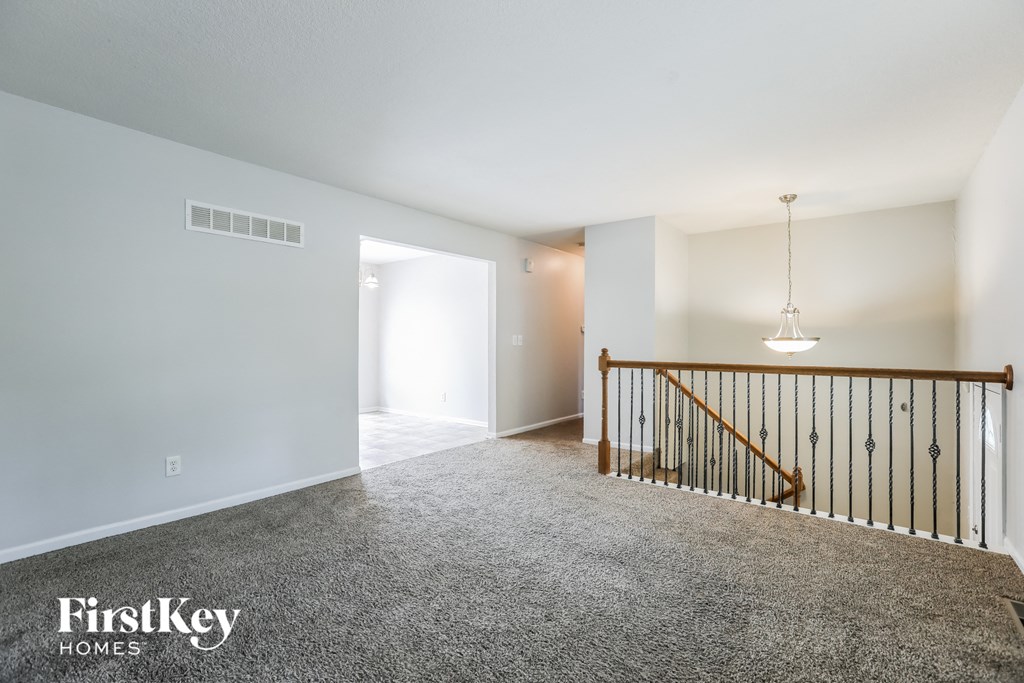 A spacious room with a carpeted floor and a wooden staircase.