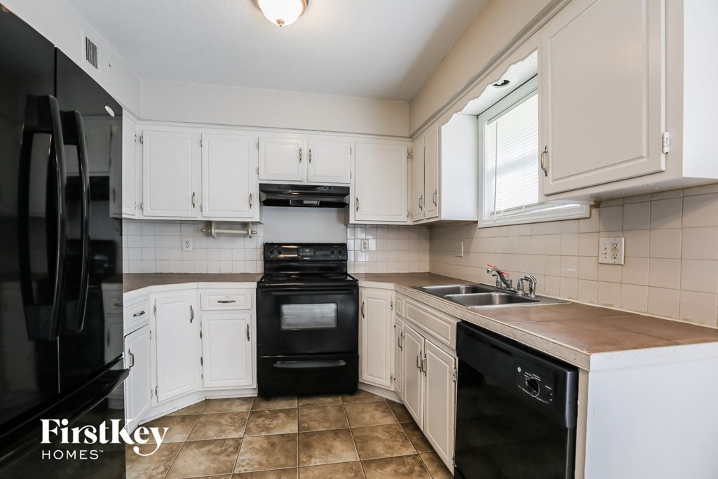 A kitchen with white cabinets and a black fridge.