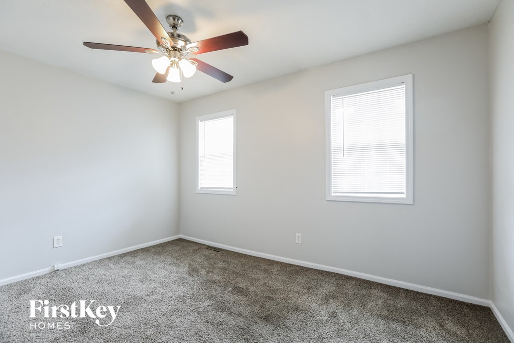 A room with a ceiling fan and two windows.