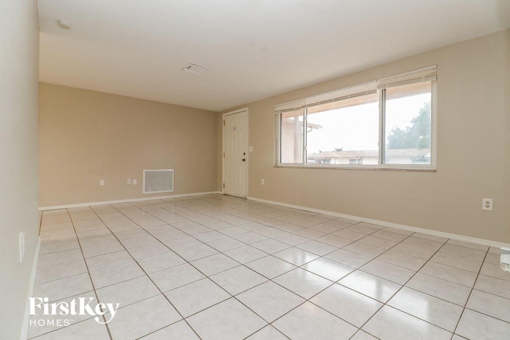 an empty living room with a large window and tiled floors