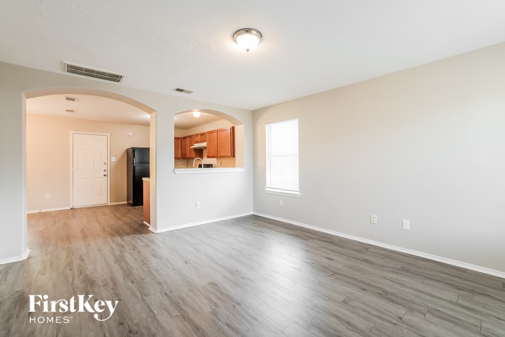 A spacious room with wooden flooring and a kitchen area in the background.