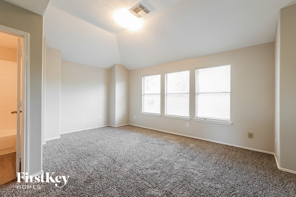 A spacious room with a grey carpet and a window.