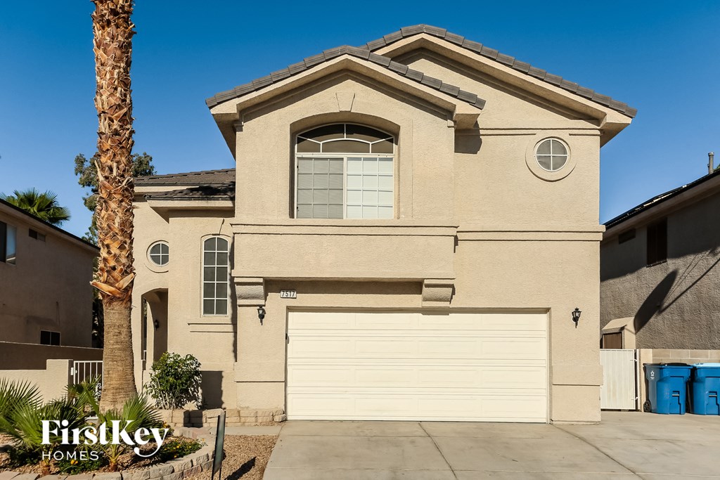 A beige house with a garage door and a palm tree in front.