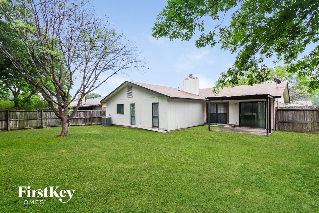 a backyard with a white house and a grass yard and a fence