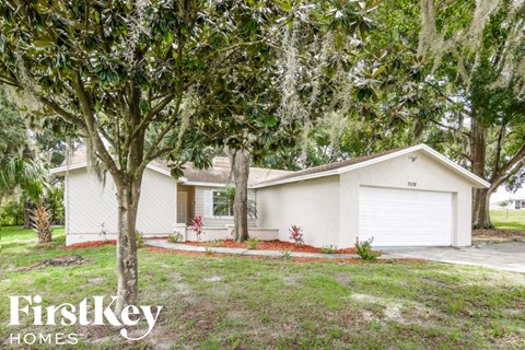 A white house with a garage is surrounded by greenery.