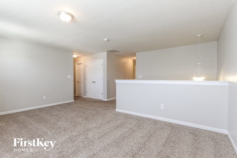 a spacious living room with white carpet and a white kitchen