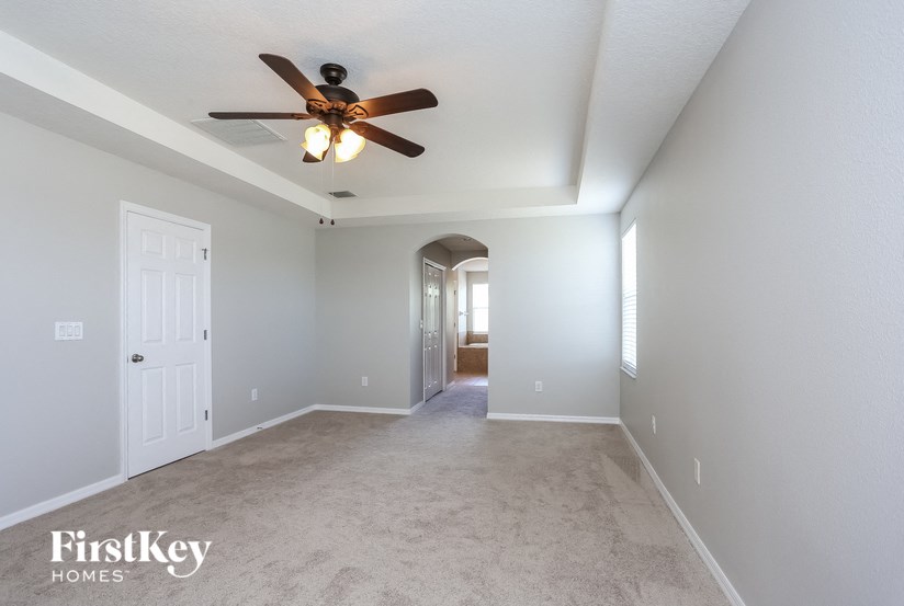A spacious room with a ceiling fan and light fixture, and a door on the left.