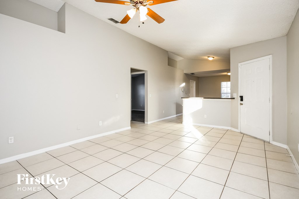 an empty living room with white tile flooring and a ceiling fan
