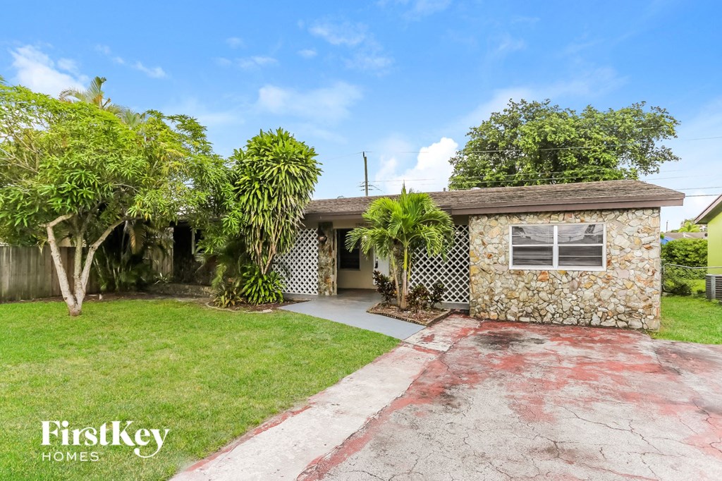 a small brick house with a driveway and palm trees