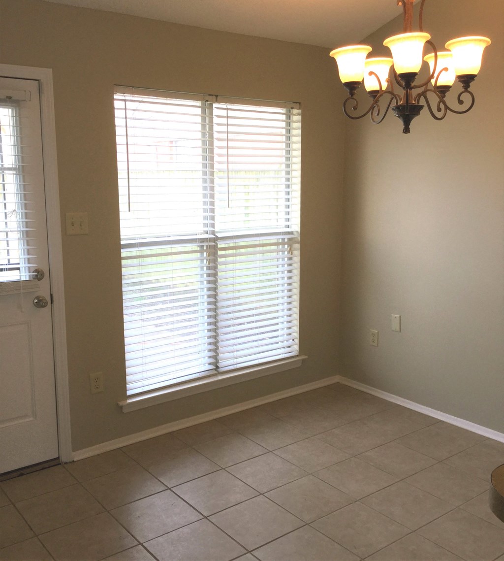 A room with a chandelier, tiled floor, and a window with blinds.