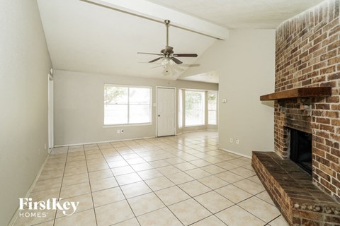 A spacious living room with a brick fireplace and a ceiling fan.